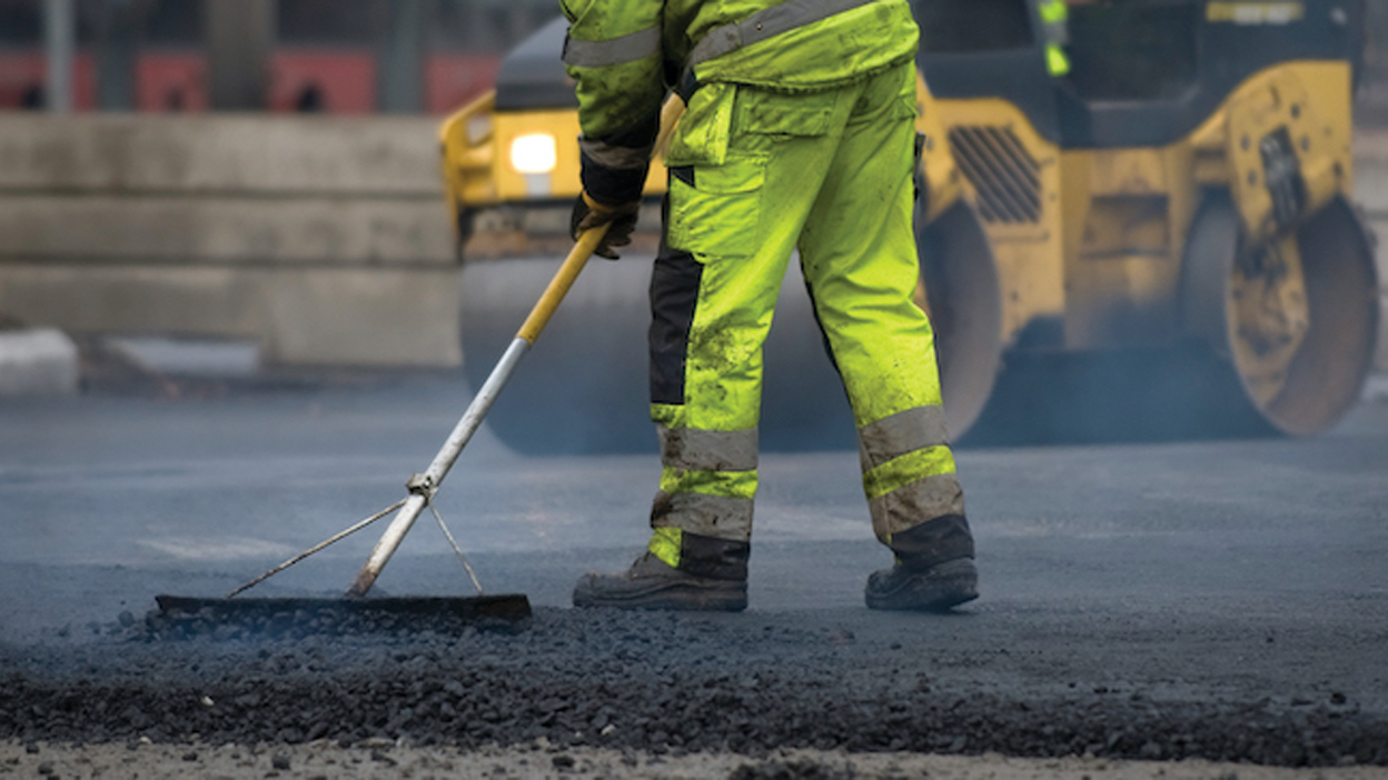 Male resurfacing road wearing hi-visibility work trousers and jacket